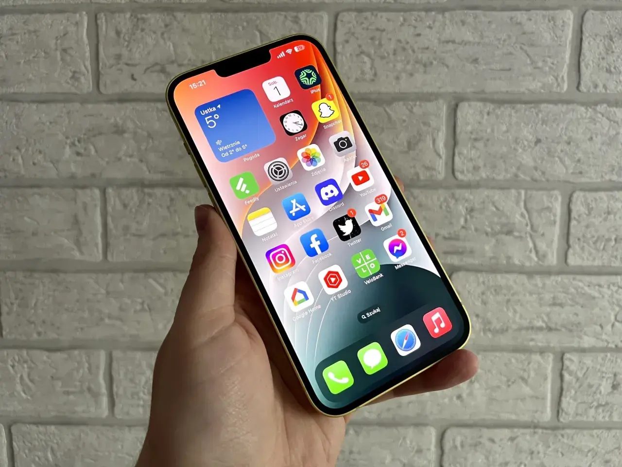 Złoty iPhone z widokiem na ekran główny, gdzie widać aplikacje takie jak pogoda, kalendarz, zdjęcia, YouTube, Gmail. Idealny do codziennej komunikacji i rozrywki, a także do wymiany informacji.