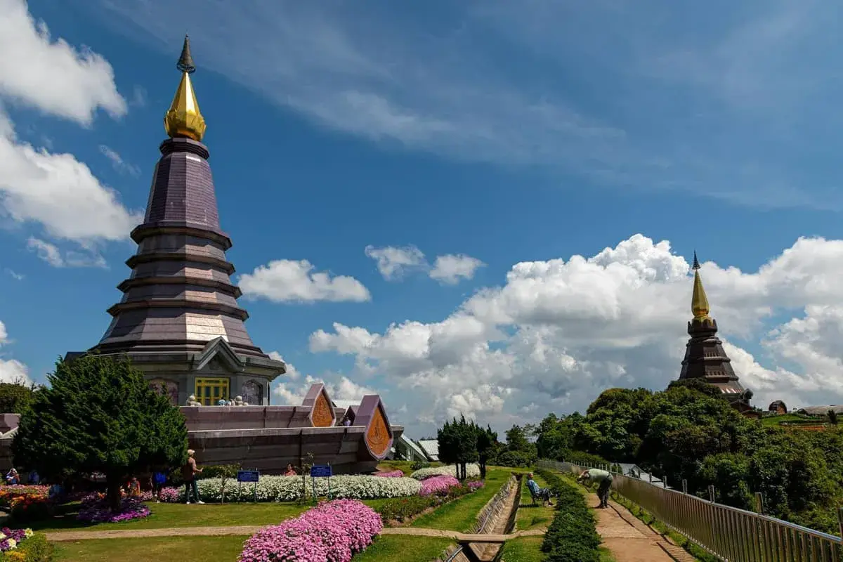 Dwa pagody na szczycie Doi Inthanon National Park, otoczone kwitnącymi kwiatami i bujną zielenią, pod błękitnym niebem z białymi chmurami.