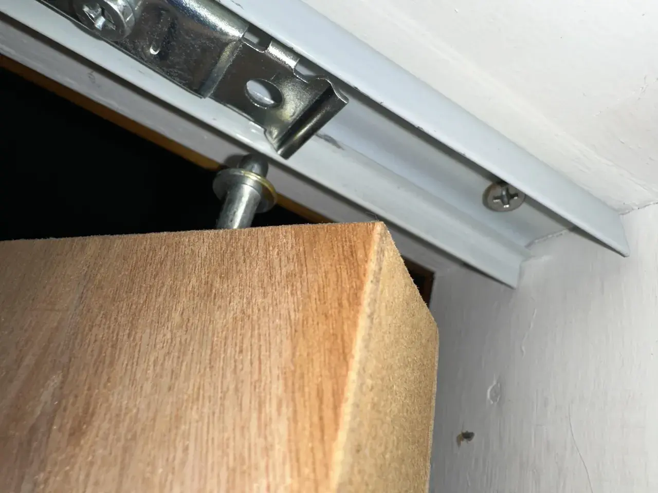Detalle de una puerta armario descolgada, con el soporte metálico visible y el borde de madera.
