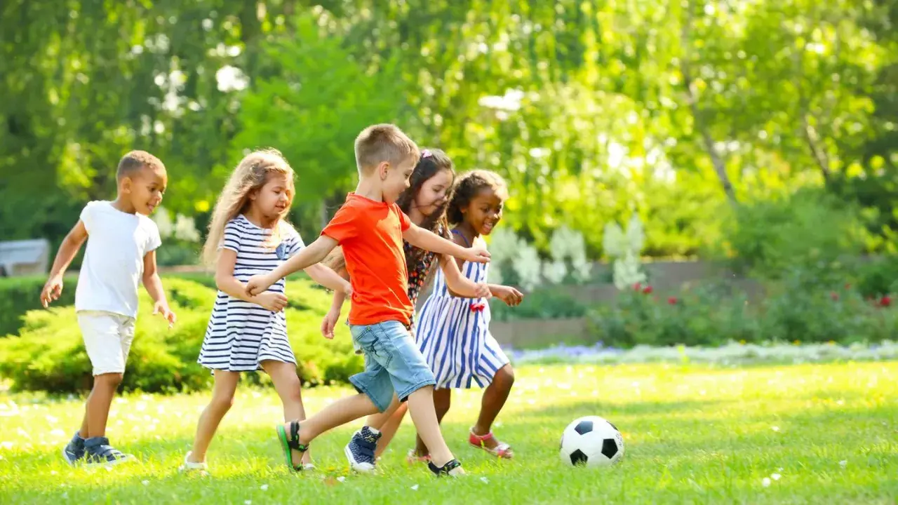 Kinder haben Spaß bei Bewegungsspielen im Kindergarten. Sie spielen Fußball auf einer sonnigen Wiese.