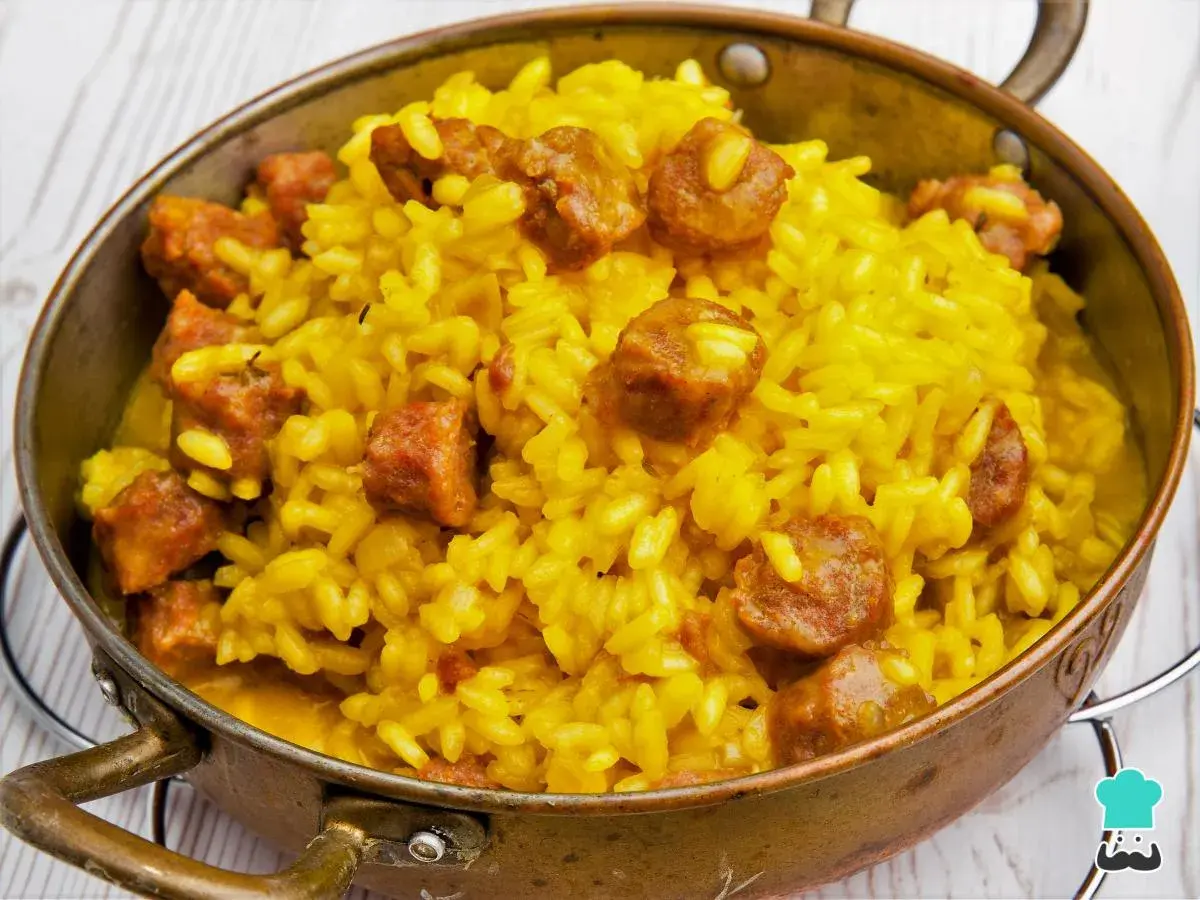 Arroz a la milanesa, un plato amarillo vibrante con trozos de salchicha, servido en un cuenco de cobre.