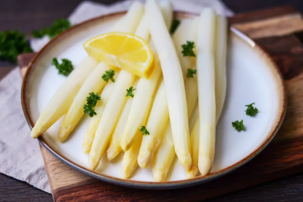 Frischer weißer Spargel, perfekt gekocht, garniert mit Petersilie und einer Zitronenspalte auf einem Teller. Ein Genuss, wenn Spargel Saison hat.
