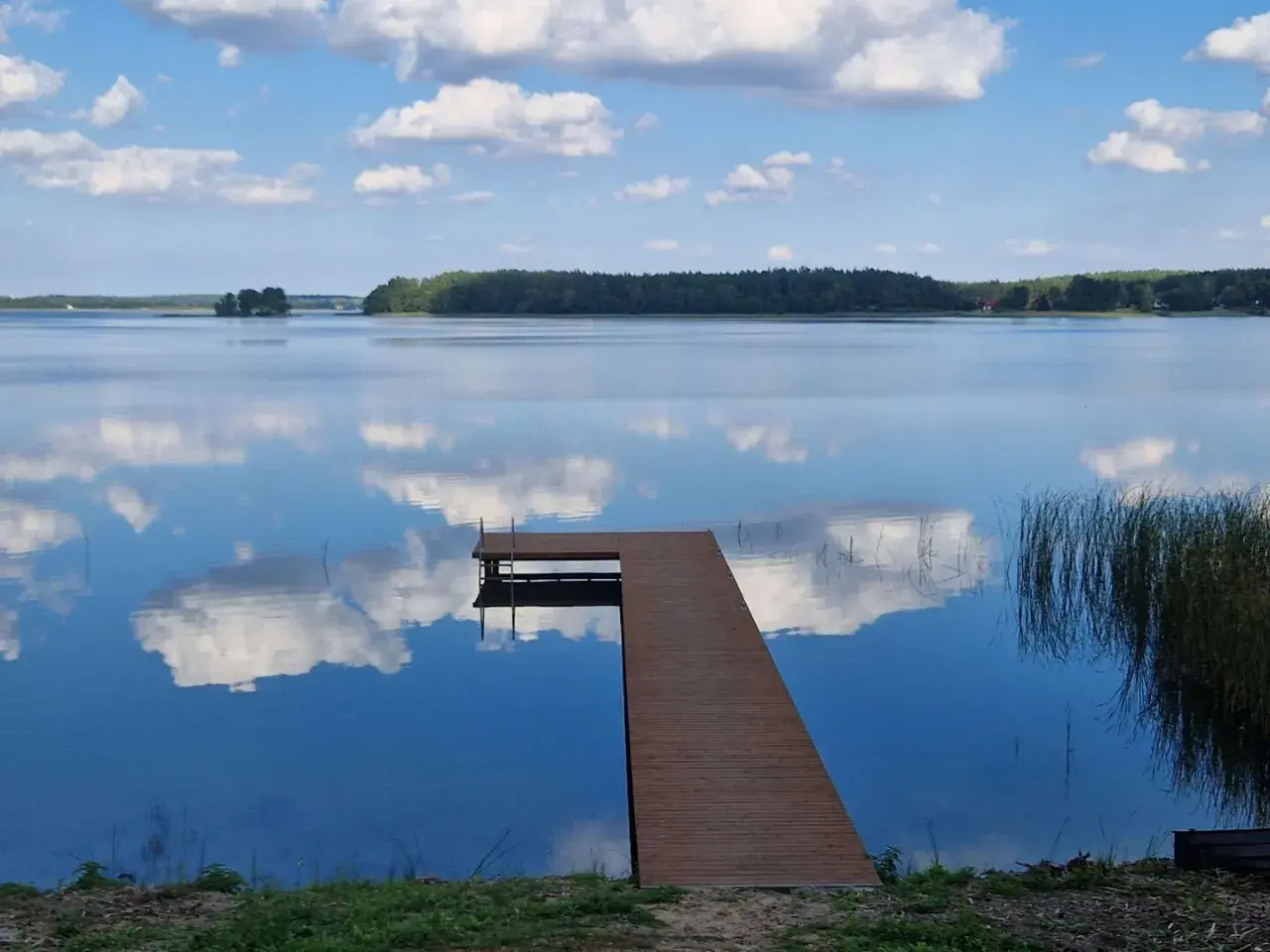 Drewniany pomost na spokojnym jeziorze przechlewskim, odbijającym błękitne niebo z białymi chmurami.