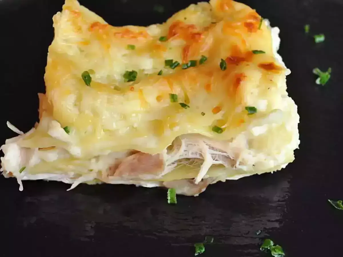 Une part de lasagnes poulet champignons, gratinée et garnie de persil frais, sur une assiette noire.