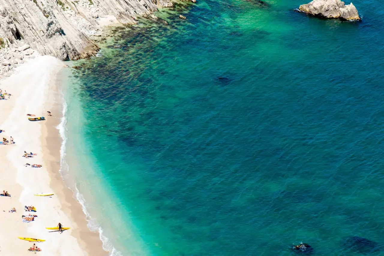 Spiaggia dorata e mare cristallino, con kayak gialli e persone che si godono il sole. Un angolo di paradiso che ricorda il **gradara mare**.