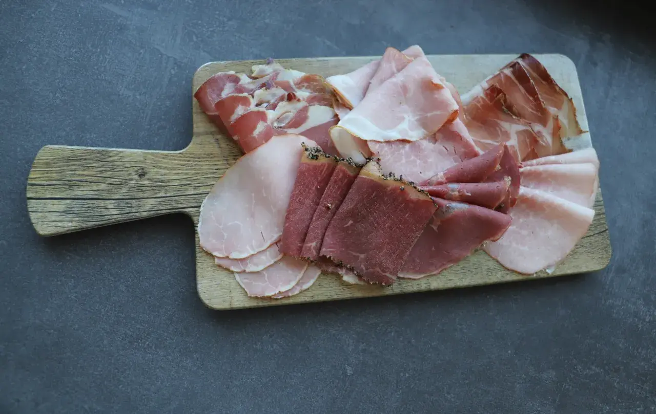 Holzbrett mit verschiedenen Aufschnittsorten, darunter zarter **prosciutto crudo**, Schinken und Rindfleisch.