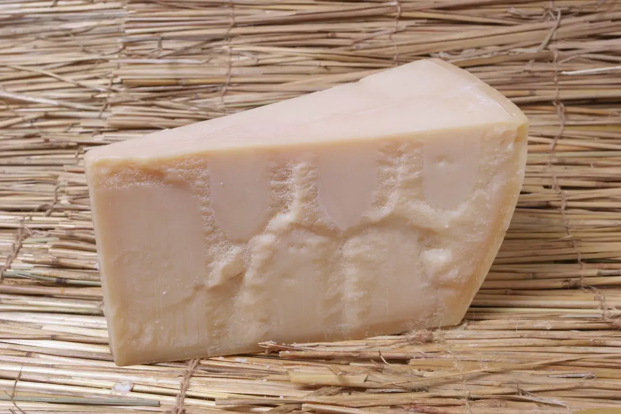 En bit Grana Padano parmesanost ligger på en bädd av halm.