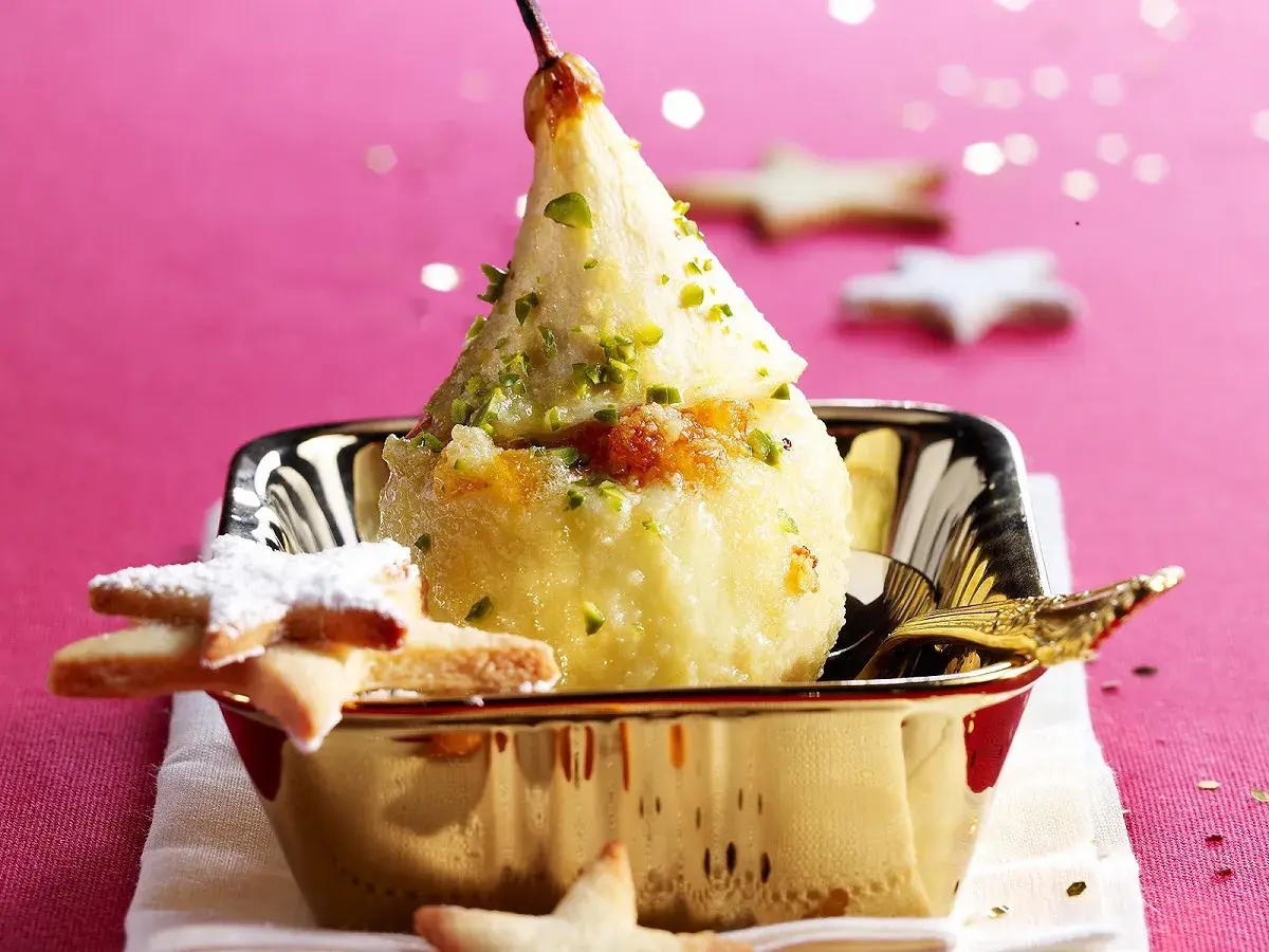 Poire pochée, garnie de pistaches et de miettes de biscuit, servie dans un bol doré. Une idée gourmande pour une recette chartreuse.