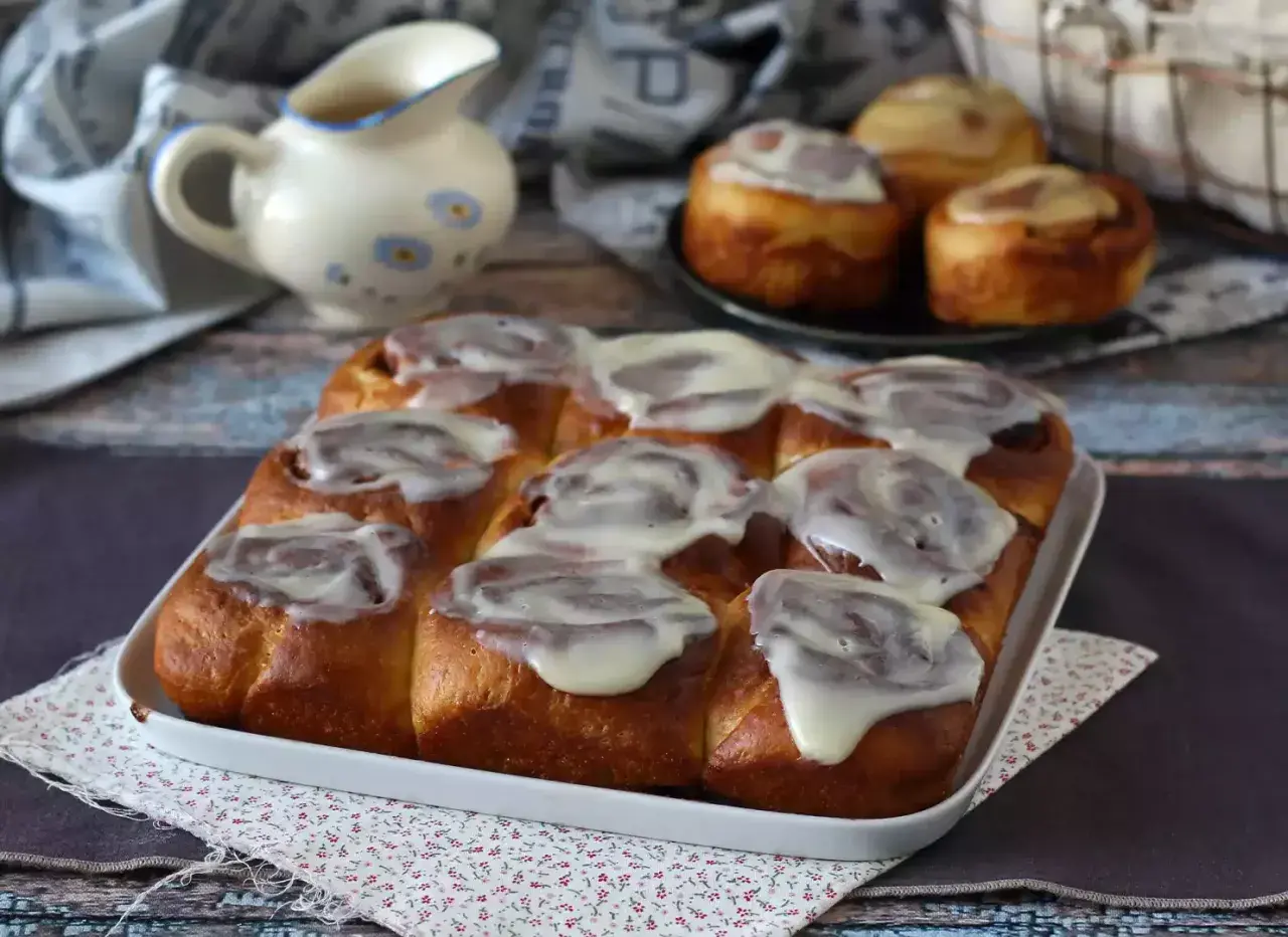 Deliciosos rollitos de canela recién horneados, cubiertos con un glaseado blanco cremoso, listos para ser disfrutados.