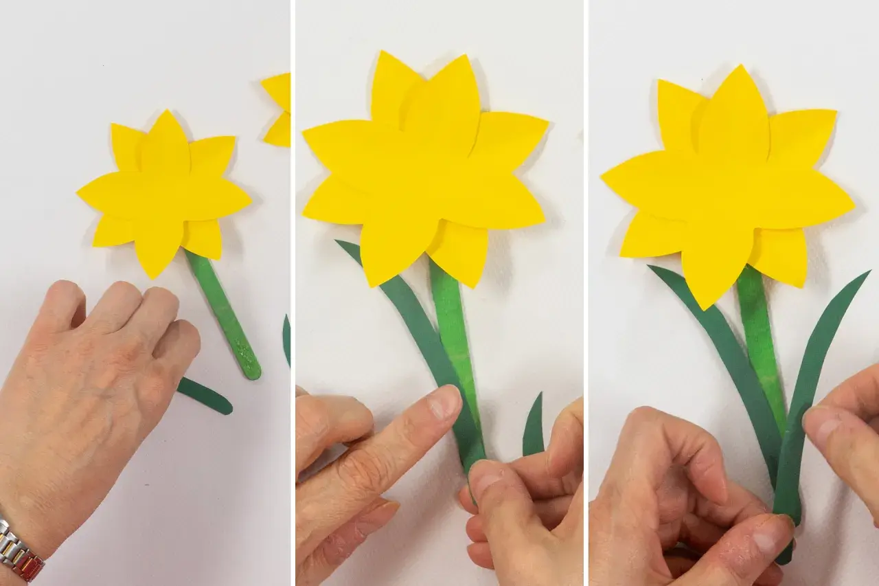Schritt-für-Schritt-Anleitung zum Narzisse basteln mit Papier. Hände kleben grüne Blätter an den Stiel einer gelben Papiernarzisse.