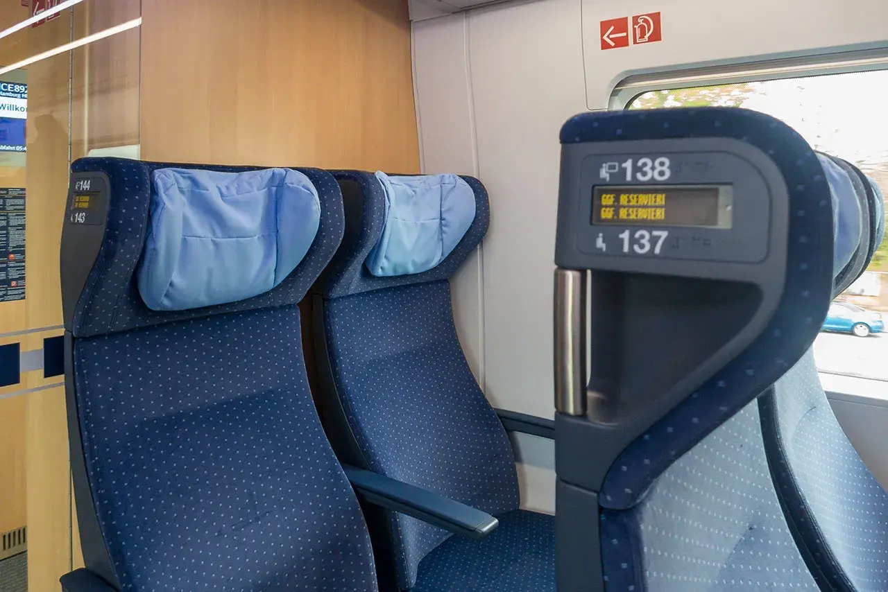 Blaue Sitze im Zug, mit Kopfkissen. Auf dem Display steht "Reserviert". Eine Reise durch Europa, vielleicht mit dem ICE.