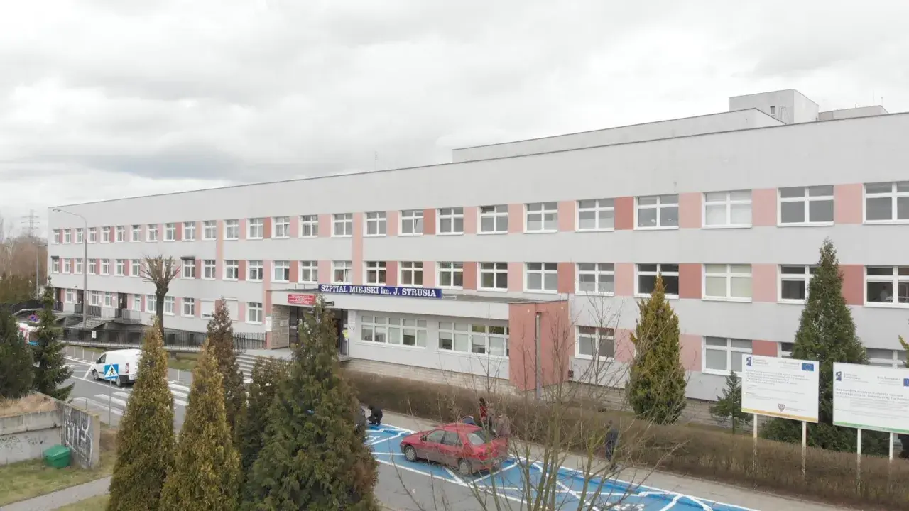 Szpital Miejski im. J. Strusia w Poznaniu. Szukasz informacji, jak dojechać do szpitala na Szwajcarskiej w Poznaniu? Budynek z wieloma oknami, przed którym rosną drzewa.