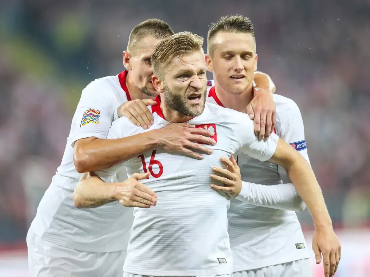 Trzech kapitanów reprezentacji Polski w białych strojach świętuje bramkę.
