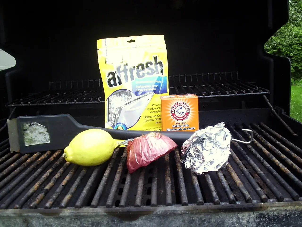 Sur la grille barbecue, un citron, un oignon, du papier aluminium, un nettoyant pour lave-vaisselle et du bicarbonate de soude.