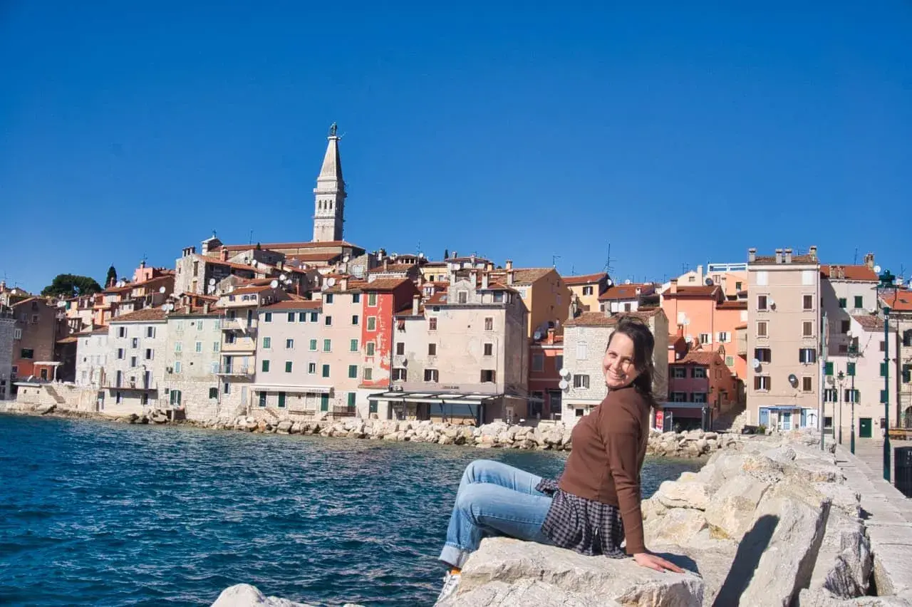 Frau sitzt auf Felsen mit Blick auf die Küstenstadt Rovinj in Kroatien.