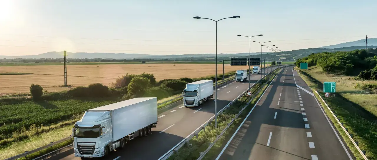 Ciężarówki na autostradzie, symbol nowoczesnych systemów monitorowania ładunków w transporcie. Słońce zachodzi nad polami.