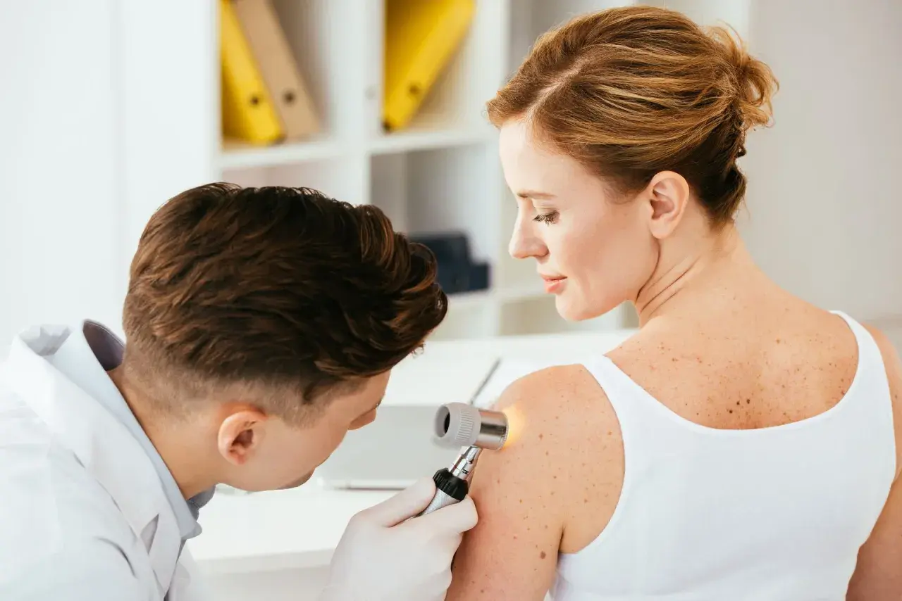 Dermatolog bada pieprzyk na ramieniu pacjentki. Warto pamiętać o samobadaniu skóry, by wcześnie wykryć czerniak na dziąśle lub innym miejscu.