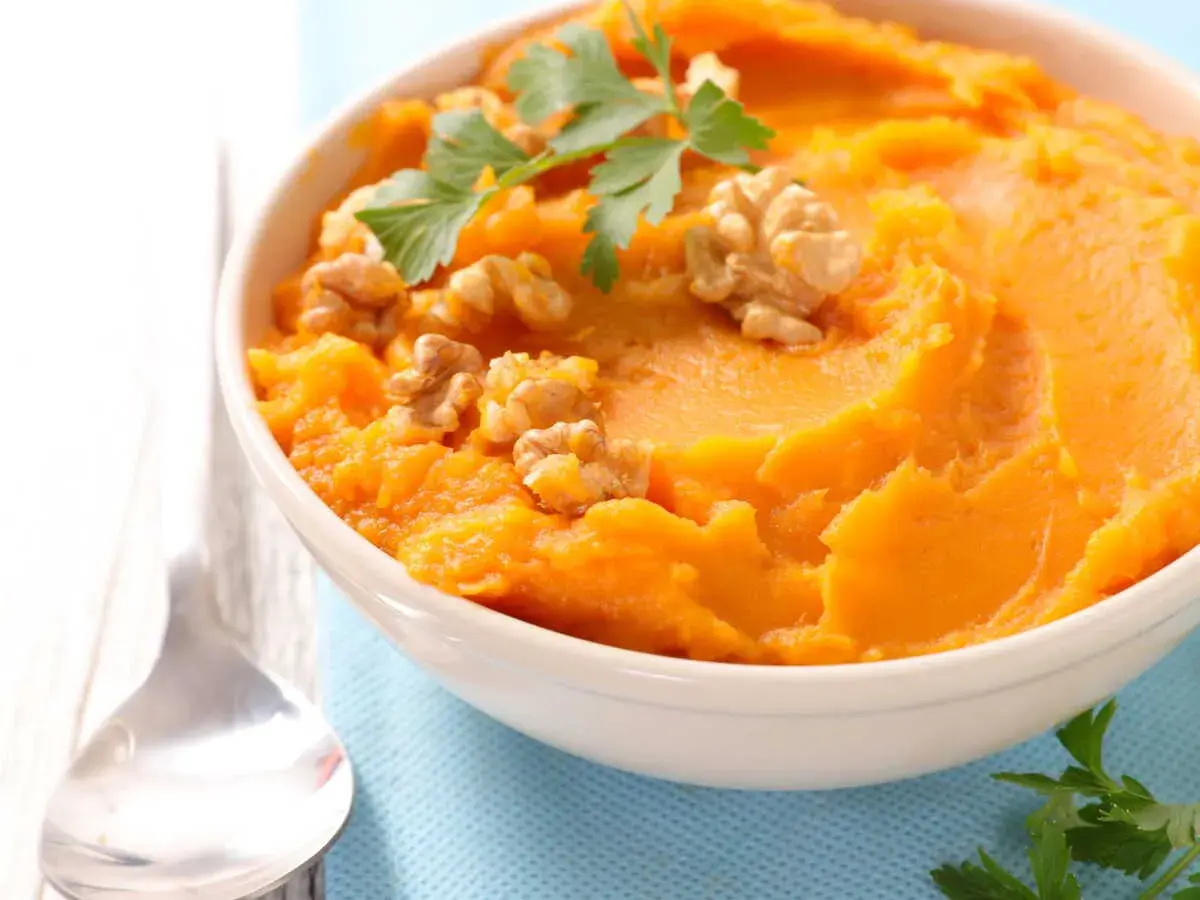 Un bol de purée de patate douce onctueuse, garni de noix croquantes et de persil frais. Un délice réconfortant.
