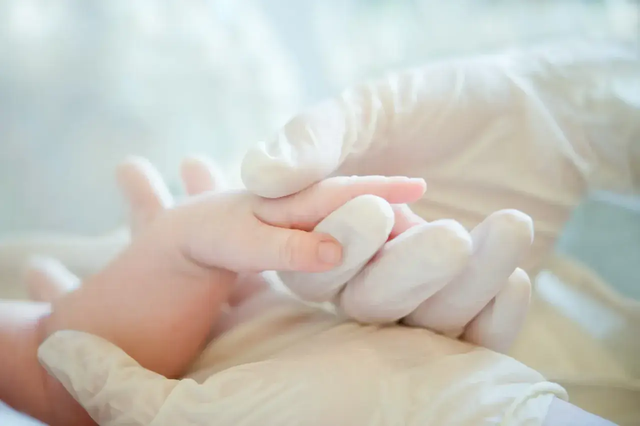 Mani guantate che tengono delicatamente un neonato, un simbolo di cura e attenzione per i possibili danni neurologici da parto.