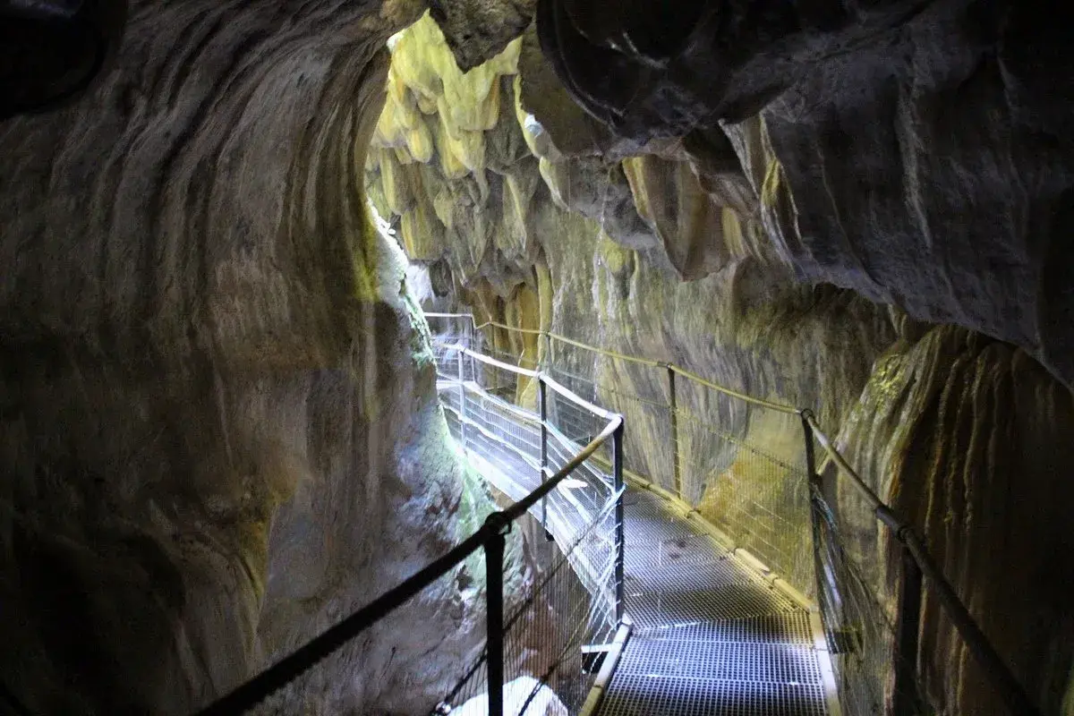 Pasarela metálica serpentea por el interior de los Gorges de la Fou, con paredes rocosas esculpidas por el agua y la luz filtrándose desde arriba.