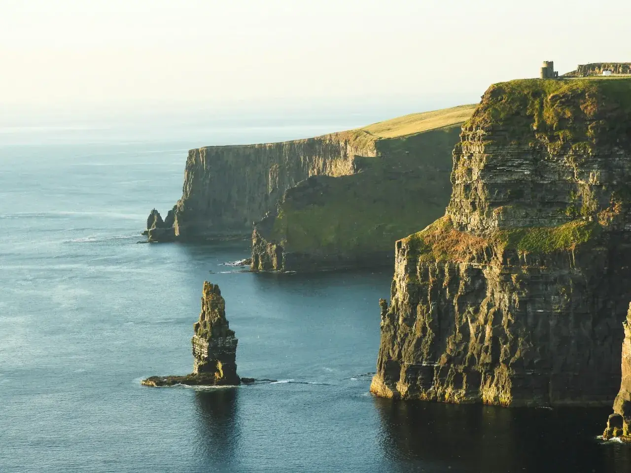 Klify Moheru – obowiązkowy punkt na mapie "Irlandia co zobaczyć". Majestatyczne skały wpadające do oceanu, z wieżą widoczną na szczycie.