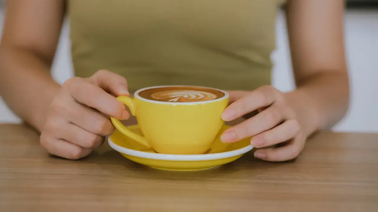 Po treningu zasłużona kawa. Jasnożółta filiżanka z latte art na drewnianym blacie.