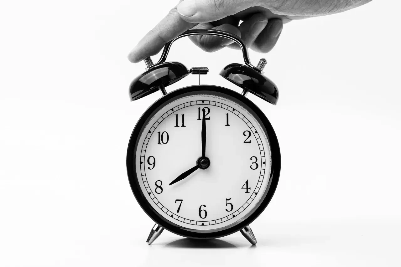 Dłoń naciska na budzik, symbolizując przekroczenie czasu pracy i potencjalny mandat.