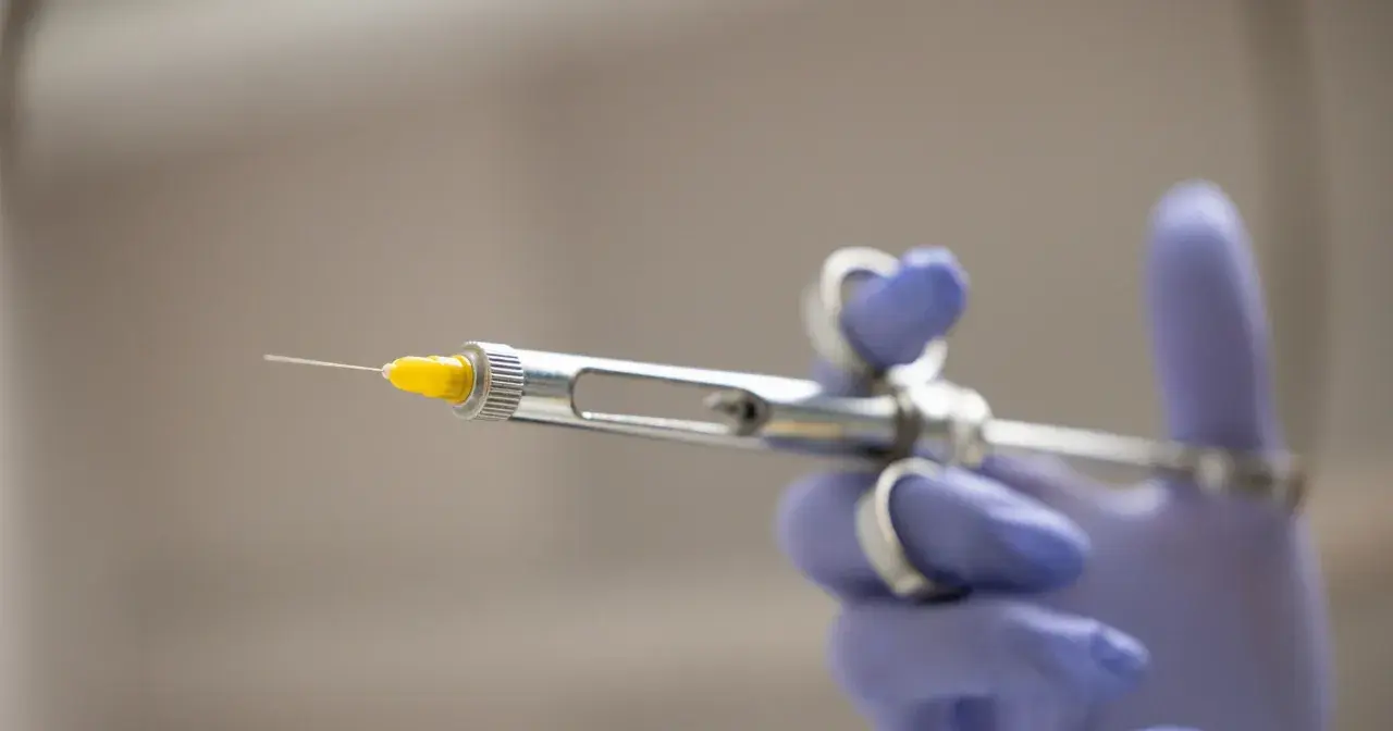 Dłoń w fioletowej rękawiczce trzyma strzykawkę dentystyczną. Co zrobić, gdy znieczulenie nie schodzi? Skonsultuj się z dentystą.