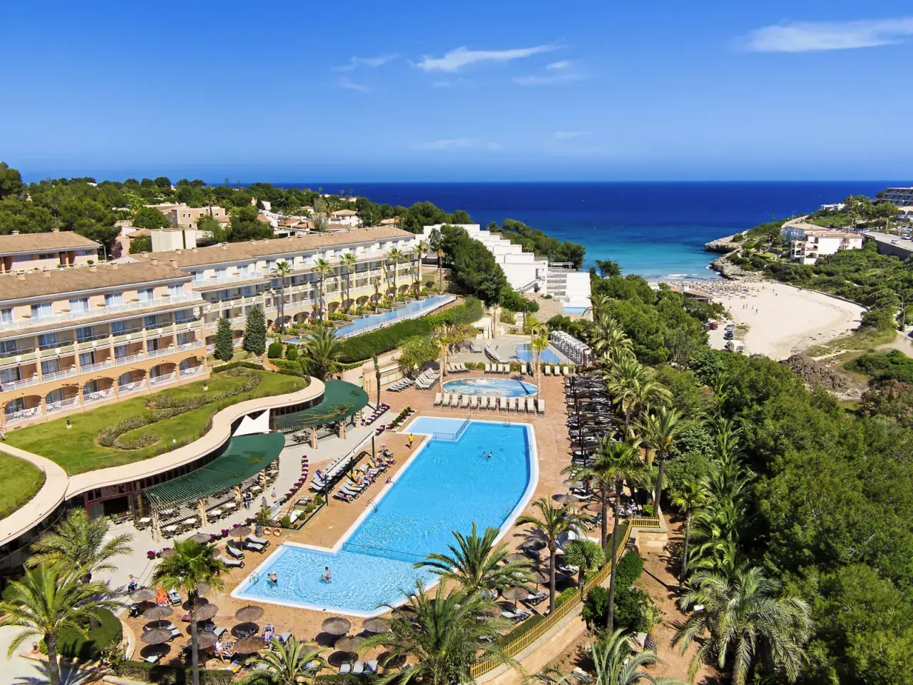 Blick auf das TUI Kids Club Cala Mandia Resort mit Pools, Strand und Meer.