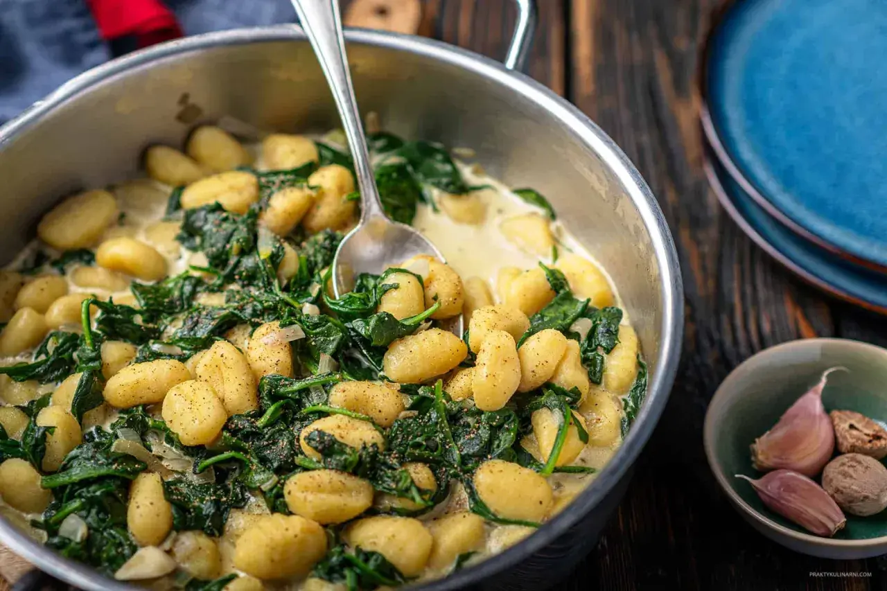 Gnocchi ze szpinakiem w kremowym sosie, podane w metalowej patelni, obok czosnku i gałki muszkatołowej.