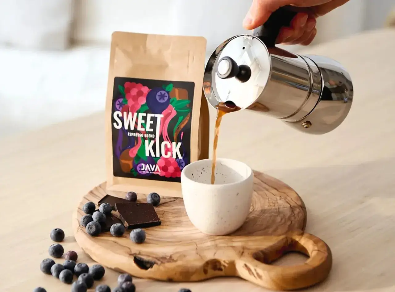 Kawa "Sweet Kick" z kawiarki nalewana do filiżanki. Na desce leżą jagody i czekolada. Idealna ilość kawy do kawiarki.