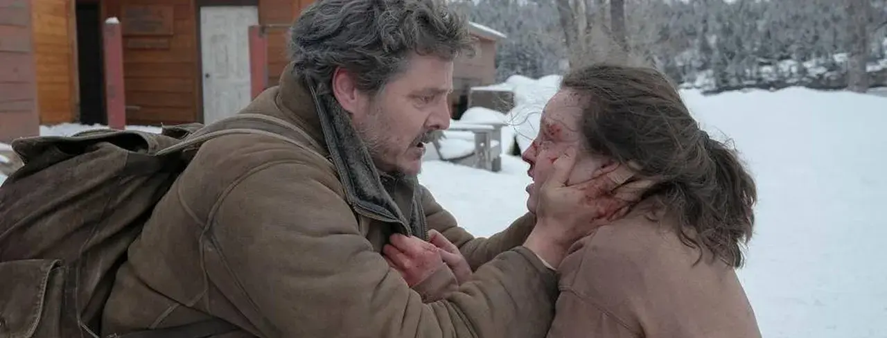 Joel w śnieżnej scenerii, z krwawymi śladami na twarzy, trzyma za podbródek rannego Ellie. To mocna scena, która pokazuje, jak ważna jest obsada w budowaniu napięcia.