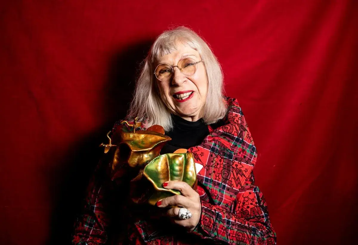 Suzanne på scen, glad och med ett glittrande pris i famnen, klädd i en röd rutig kavaj mot en röd bakgrund.