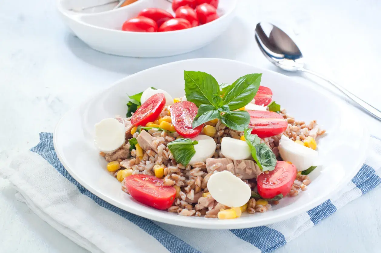 Deliziosa insalata di orzo con tonno, pomodorini, mais e mozzarelline, guarnita con basilico fresco. Un piatto completo e colorato.