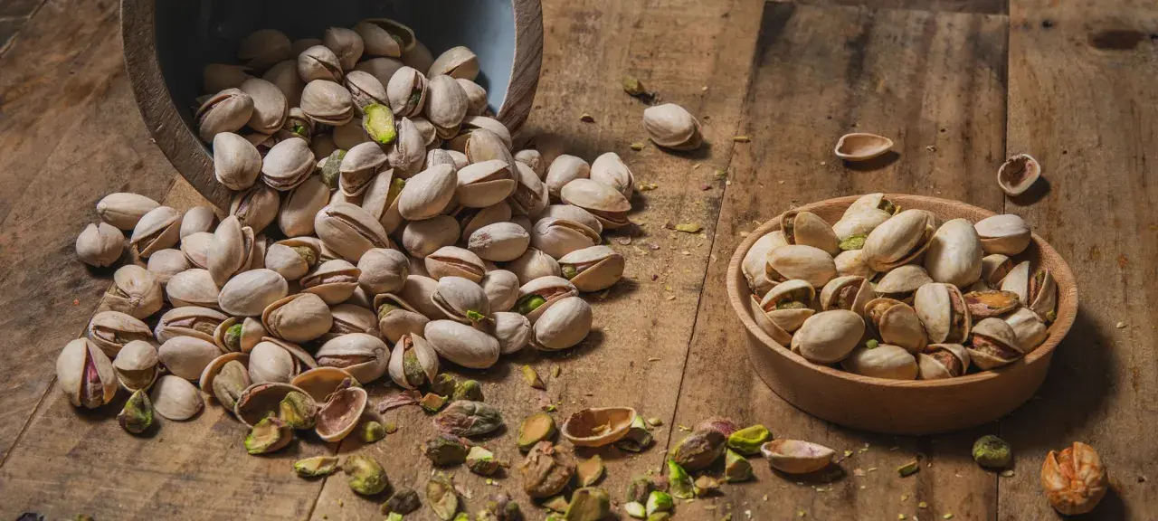 Pistacchi in una ciotola e sparsi su un tavolo di legno. Scopri le incredibili pistacchi proprietà per la tua salute.