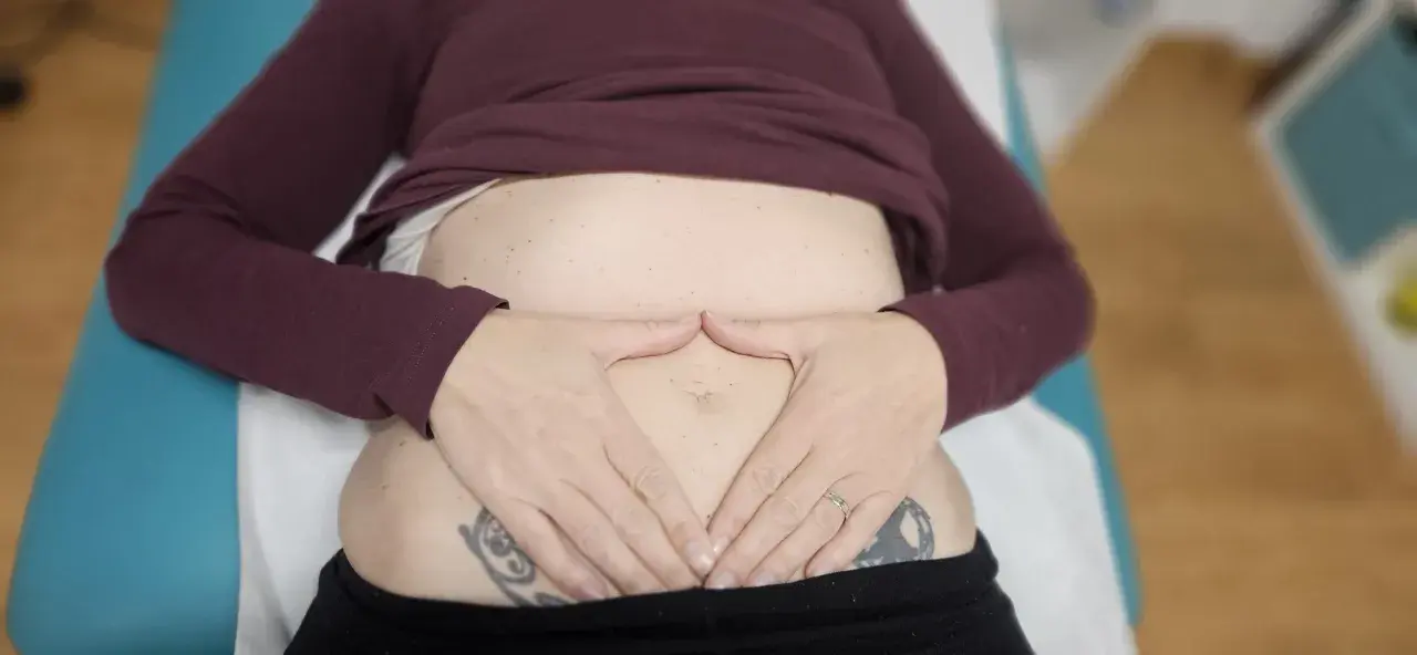 Manos sobre el abdomen, sintiendo el dolor de espalda por gases.