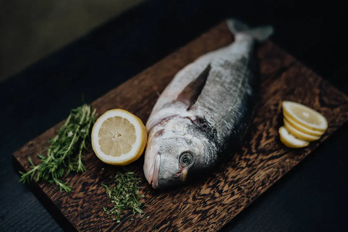 Un beau daurade prêt à être grillé, accompagné de citron frais et de romarin sur une planche en bois.