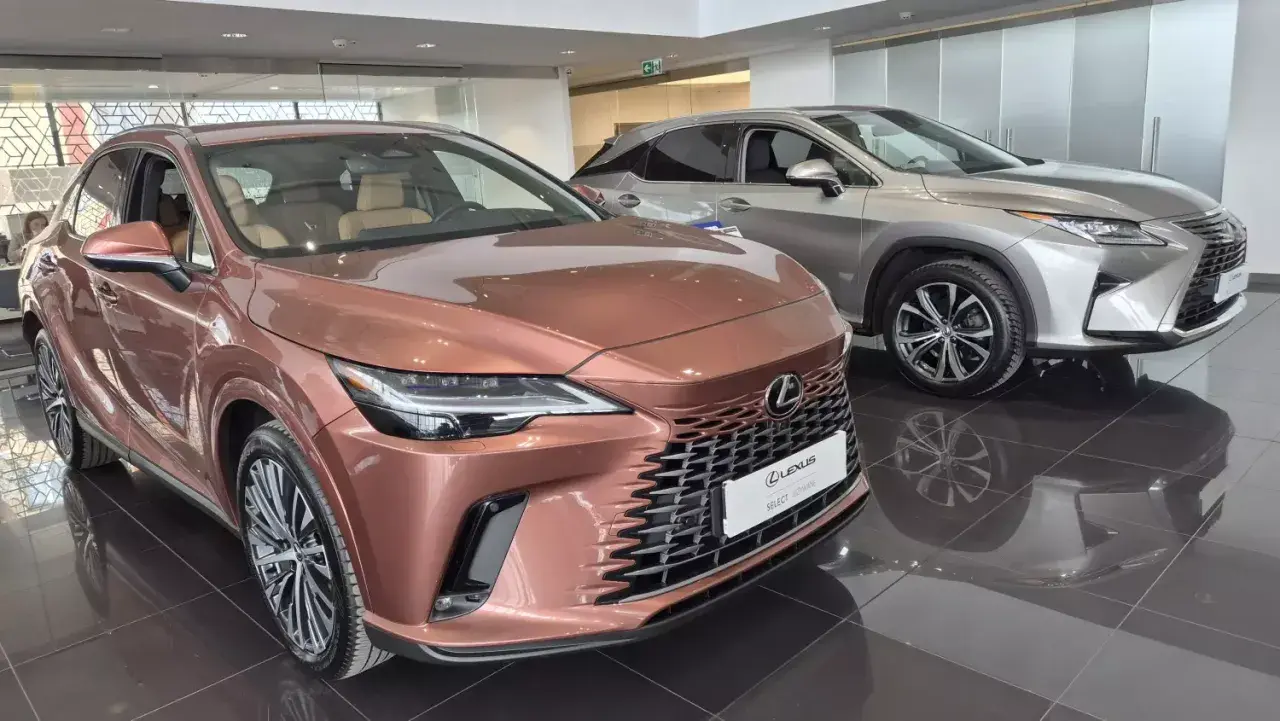 Dwa luksusowe SUV-y Lexus w salonie. Jeden w kolorze miedzianym, drugi srebrny, błyszczą na wypolerowanej podłodze.