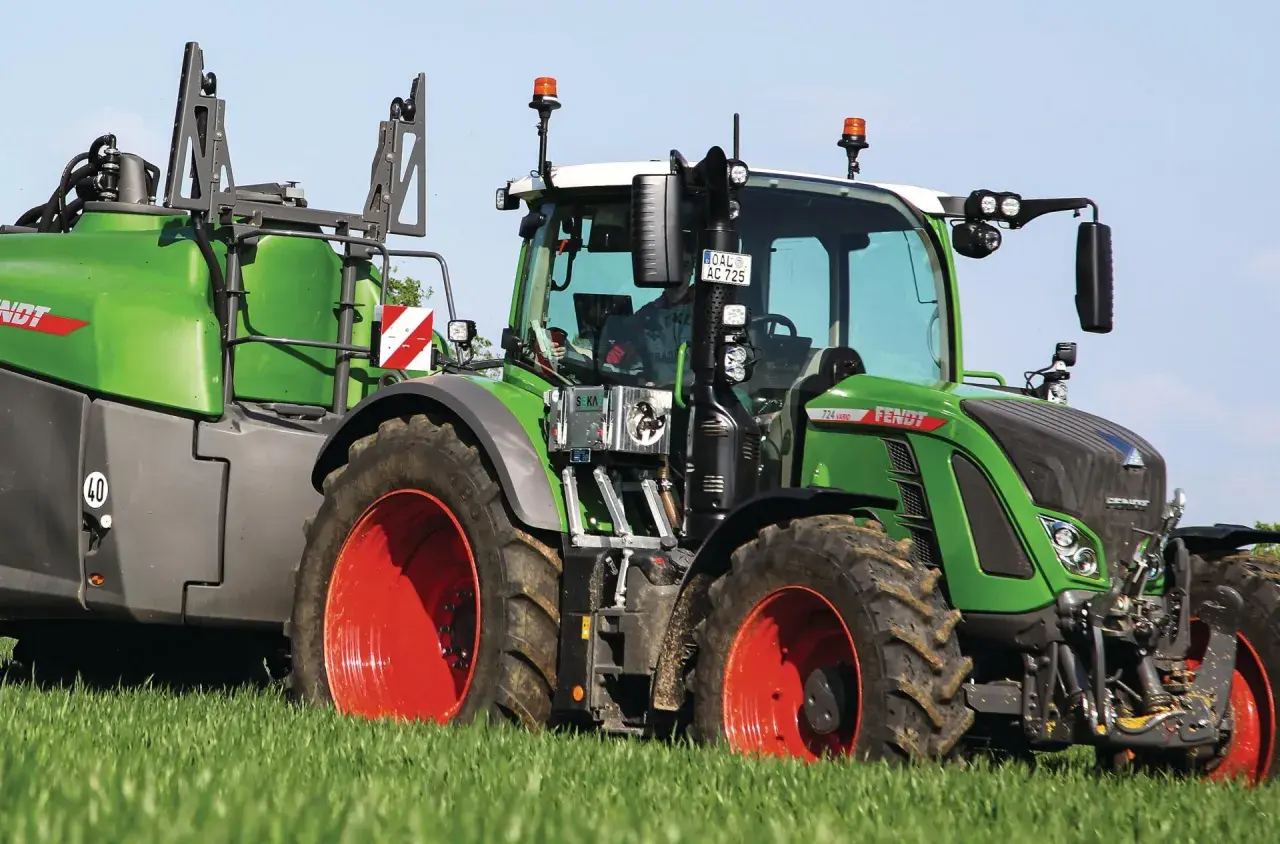 Grüner Fendt-Traktor mit Anhänger auf einem Feld. Die universellen Kabinen für Traktoren bieten Komfort und Sicherheit.