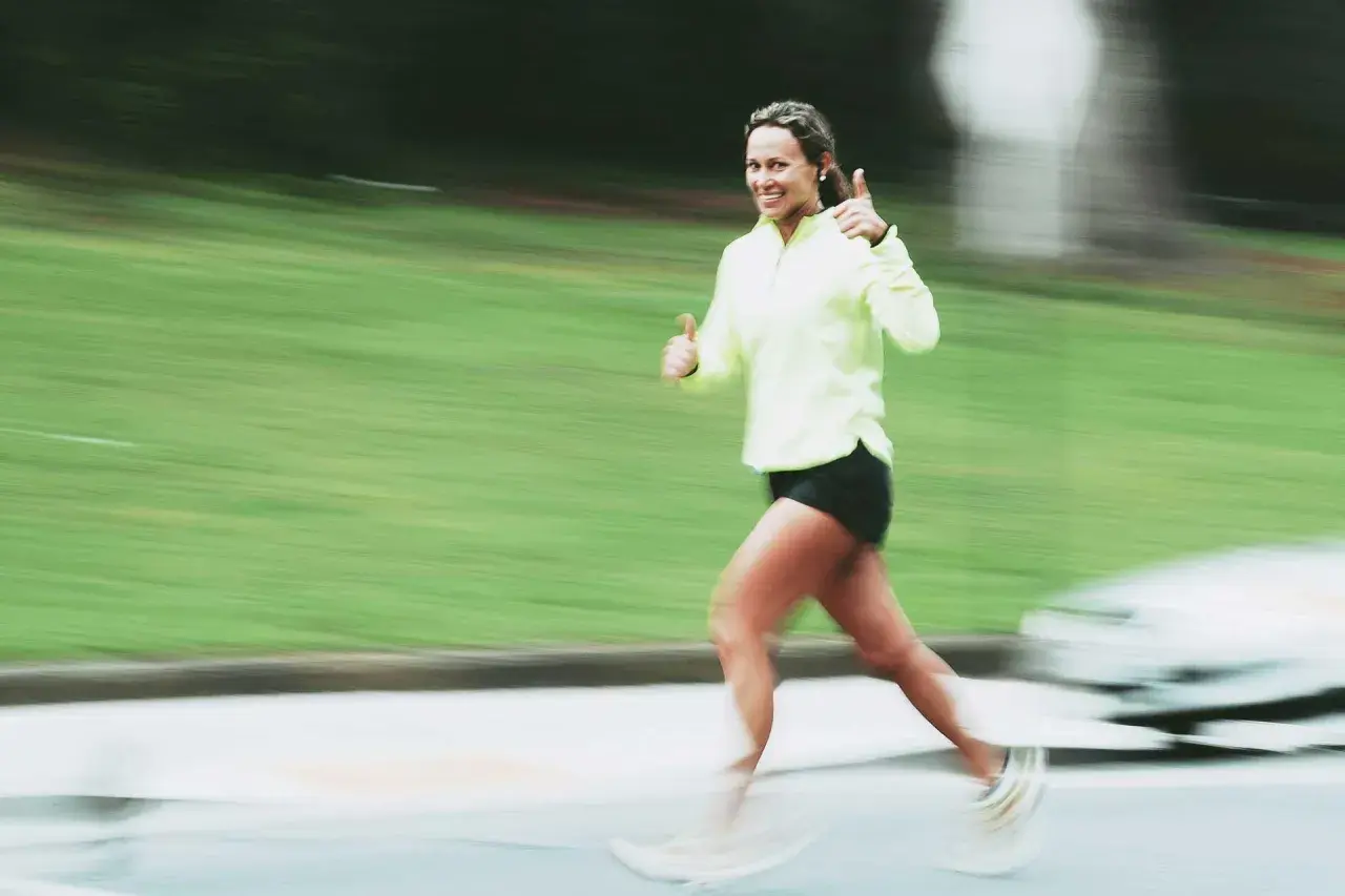 Donna sorridente corre con pollice in su, indicando un ottimo ritmo medio corsa.