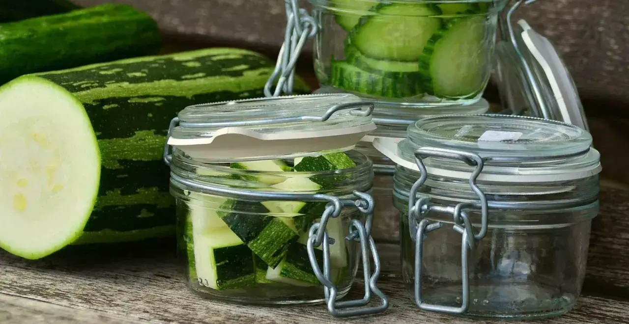 Zucchini-Scheiben und -Würfel in Gläsern, bereit zum einkochen im Dampfgarer. Frische Zucchini liegt daneben.