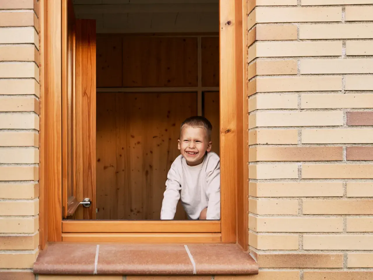Niño sonriente asoma por una ventana de madera recién instalada.