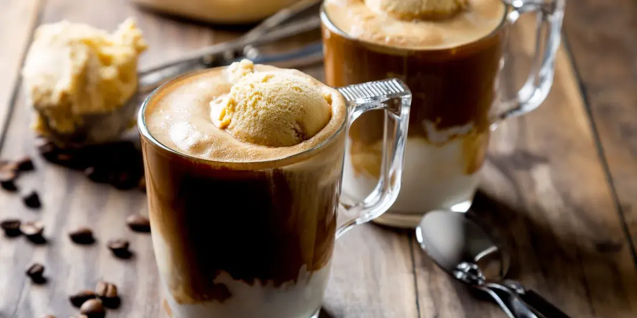 Dwa kubki caffe freddo z gałką lodów waniliowych na wierzchu, na drewnianym stole, obok ziaren kawy.