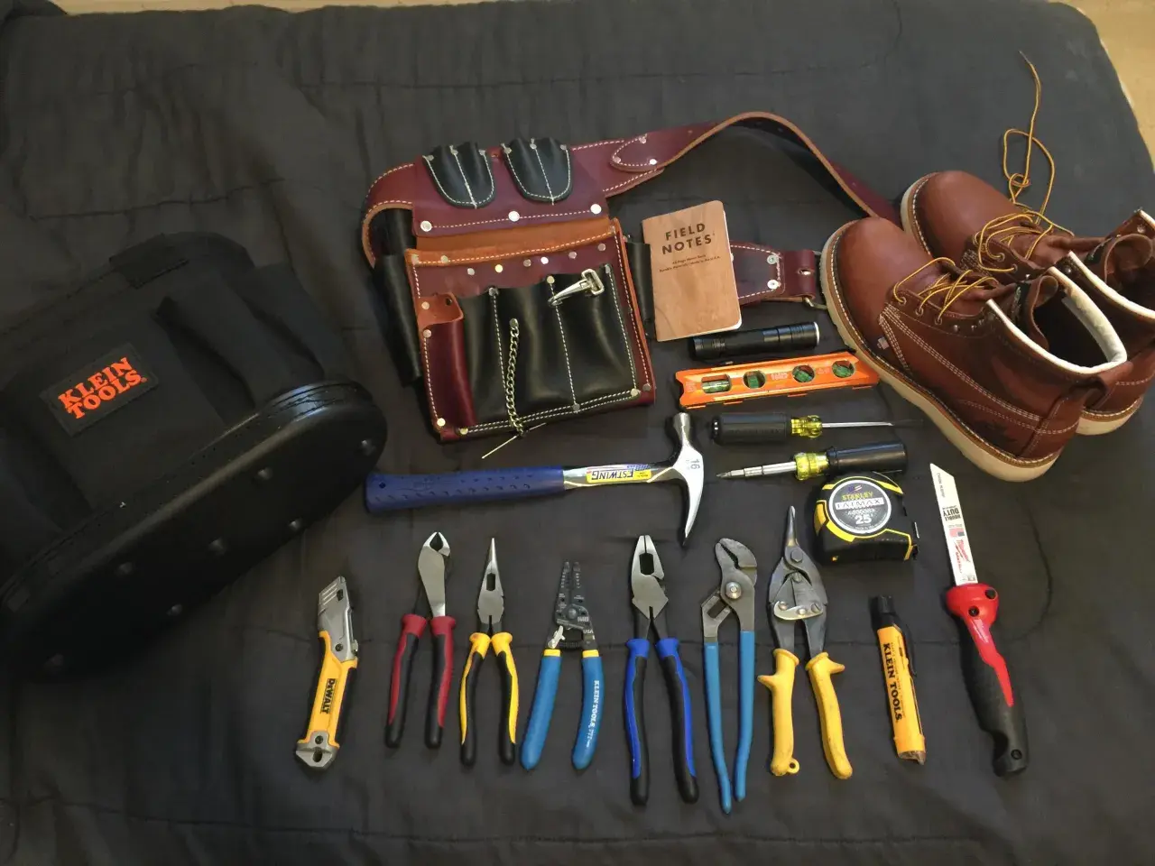 Un cinturón de cuero con múltiples compartimentos, un martillo, alicates, destornilladores, cinta métrica y botas de trabajo. Todo listo para un electricista.