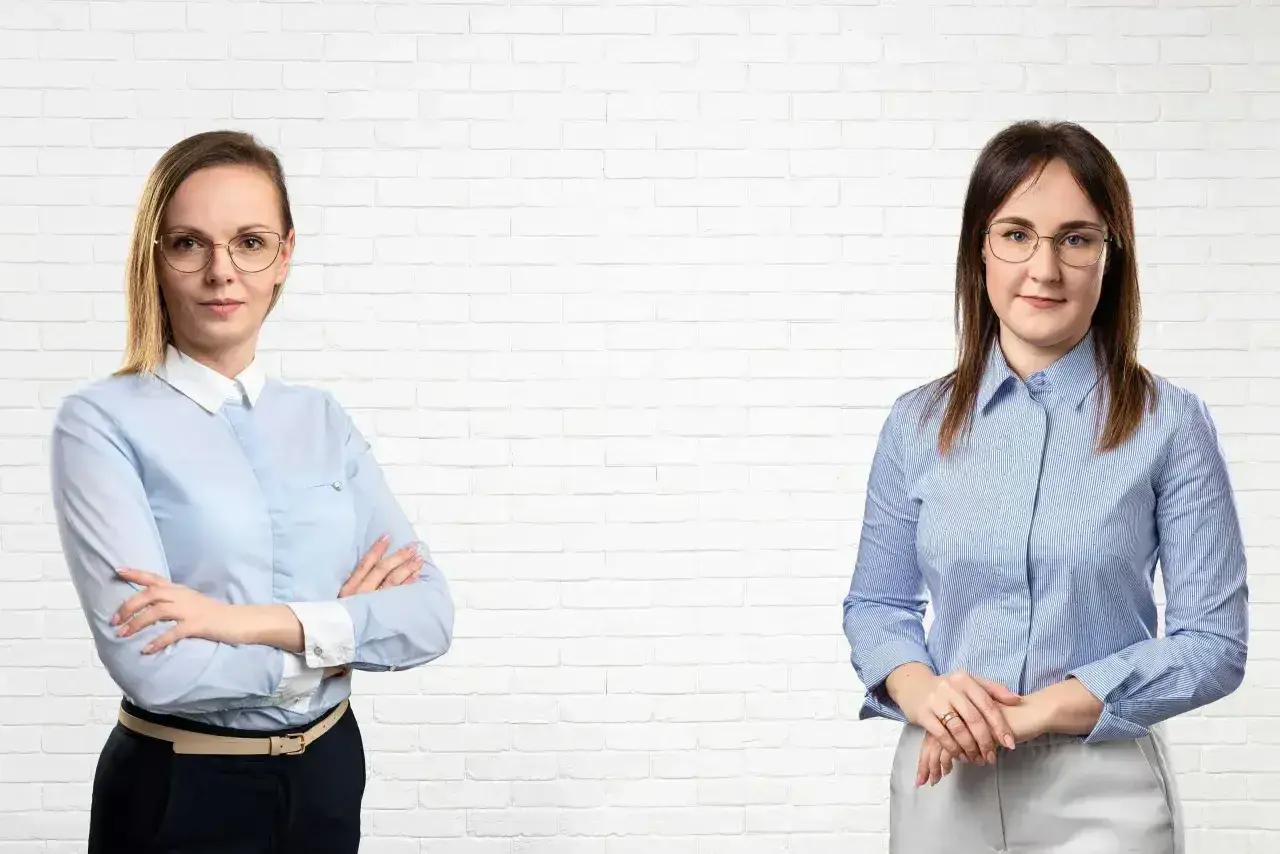 Dwie kobiety w koszulach na tle białej cegły.