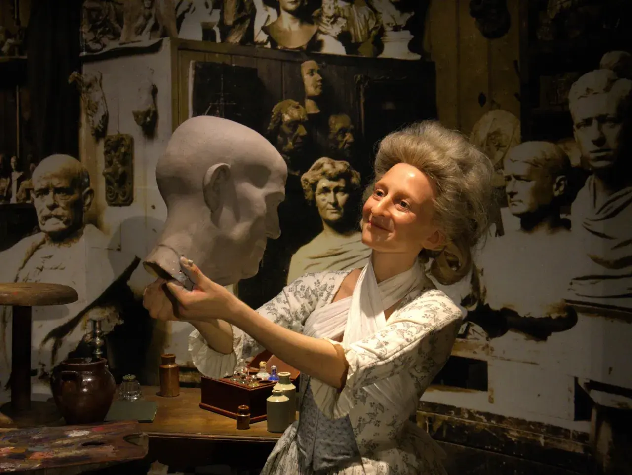 W muzeum figur woskowych artystka w historycznym stroju pracuje nad popiersiem.
