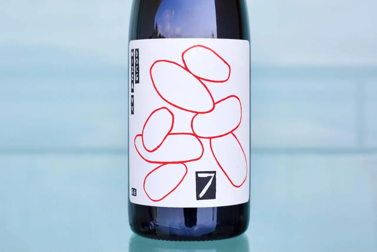 Flasche mit Etikett, das rote, abstrakte Formen und die Aufschrift "Nizza Monferrato" zeigt.