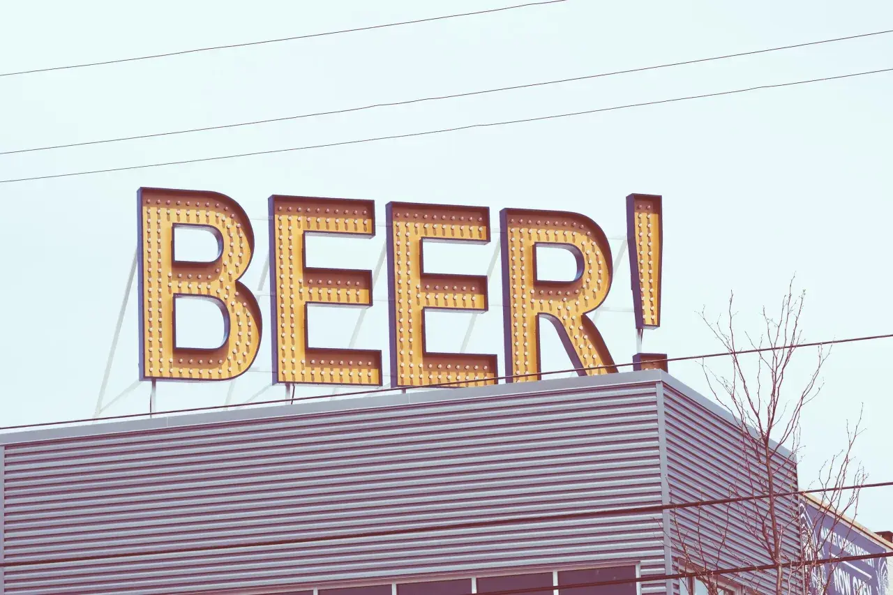 Grand panneau lumineux "BEER!" au-dessus d'un bâtiment moderne. Le nom de bière est écrit en lettres majuscules, illuminées par des ampoules.