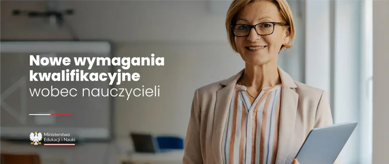 Uśmiechnięta nauczycielka w okularach trzyma tablet w sali lekcyjnej.