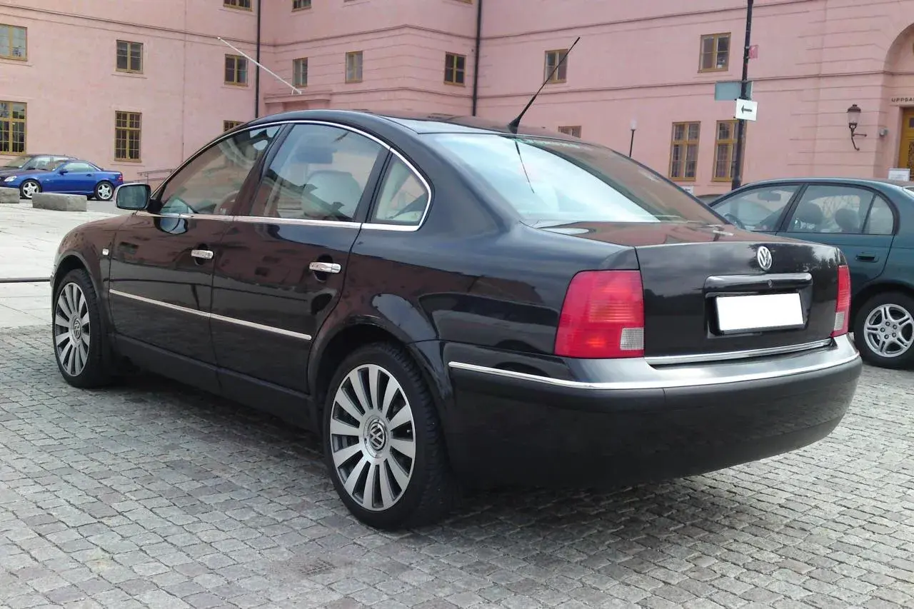 Svart Passat W8 parkerad på kullerstensgata framför en rosa byggnad.
